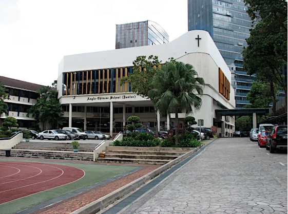 Street-level view of ACS Cairnhill Campus buildings surrounded by trees with a tall city skyscraper in the background.